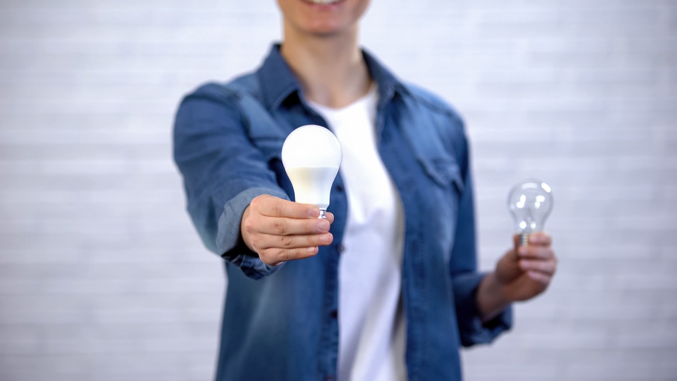 Woman holding out LED and incandescent light bulbs